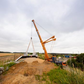Zdjęcie: pomarańczowy dźwig podnosi przęsło wiaduktu w Toszku.