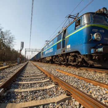 Zdjęcie: niebieski pociąg porusza się po torach.