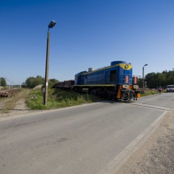 Zdjęcie: niebieski pociąg towarowy wjeżdża na przejazd kolejowo-drogowy.