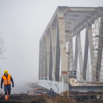 Zdjęcie: widok z ziemi na przęsło mostu na rzece Białej. Z boku idzie robotnik w pomarańczowej kamizelce.