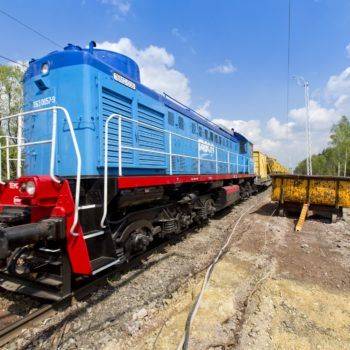 Zdjęcie: niebieski pociąg z czerwonymi detalami, w tle wagon do prac torowych.