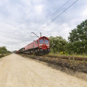 Zdjęcie: czerwony pociąg porusza się po torze, Drugi tor jest zlikwidowany i wysypany piaskiem.