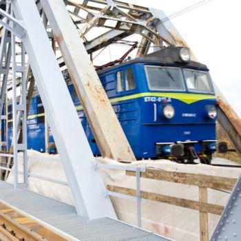 Zdjęcie: niebieski pociąg przejeżdża przez most na Wiśle.