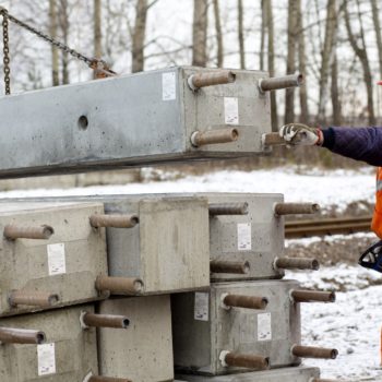 Zdjęcie: robotnik za pomocą dźwigu odkłada fundamenty palowe pod słupy kolejowe.