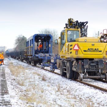 Zdjęcie: żółta koparka wyciąga nowe szyny z pociągu w którym były transportowane.