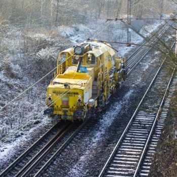 Zdjęcie: zimowy krajobraz w tle żółta maszyna do prac kolejowych.