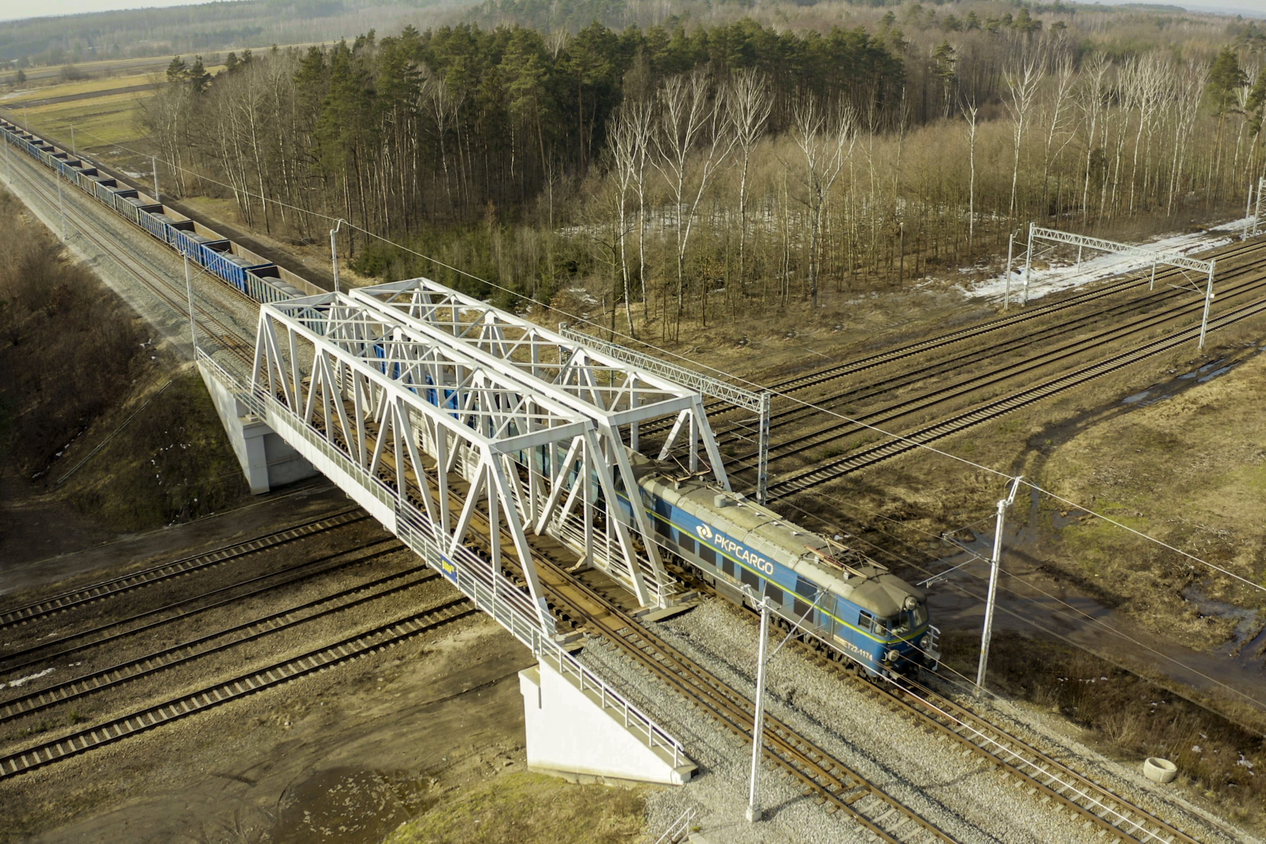 Zdjęcie: widok z góry na wiadukt kolejowo-kolejowy przez który przejeżdża pociąg.