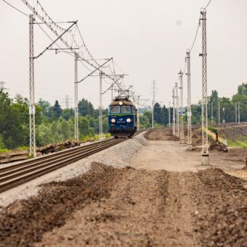 Zdjęcie: widok z ziemi na jadący pociąg przez teren budowy.