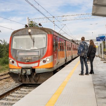 Zdjęcie: pasażerowie patrzą na nadjeżdżający pociąg.