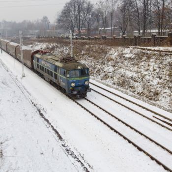 Zdjęcie: w zimowym otoczeniu przejeżdża granatowy pociąg towarowy.