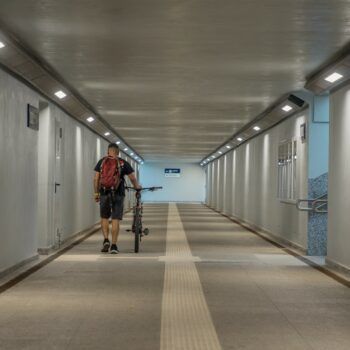 Zdjęcie: widok z poziomu ziemi na świeżo zmodernizowaną stację kolejową Oświęcim. W kadrze wnętrze tunelu podziemnego i pasażera z rowerem.